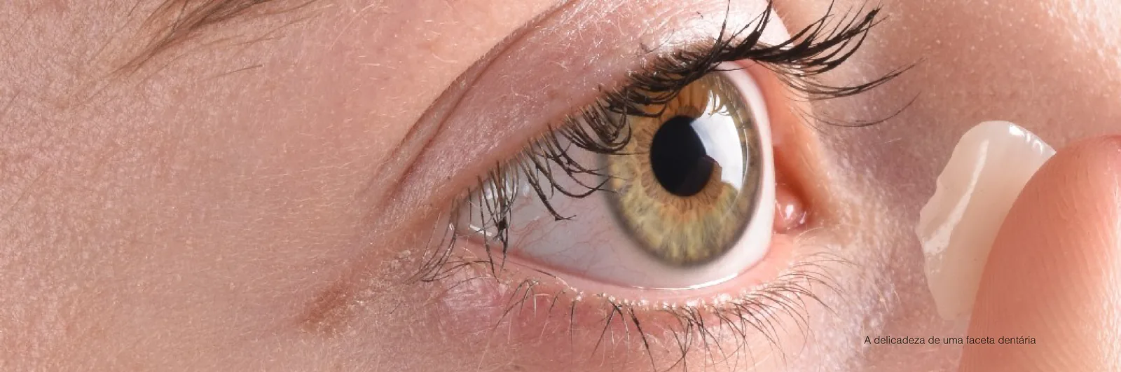 A ceramic veneer of minimal thickness, held between the fingers beside an eye, for scale comparison with a contact lens.